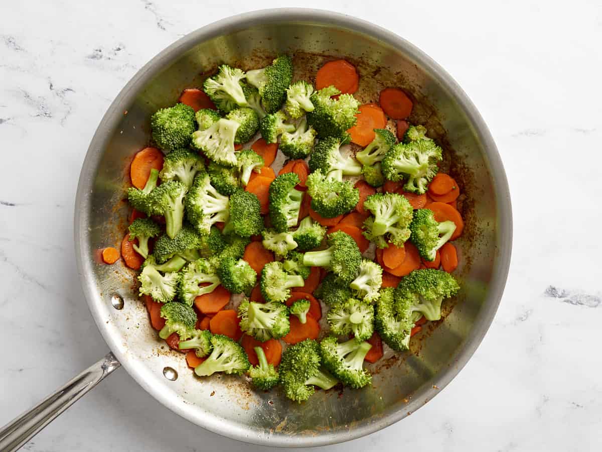 Broccoli and carrots being sautéed in a skillet.