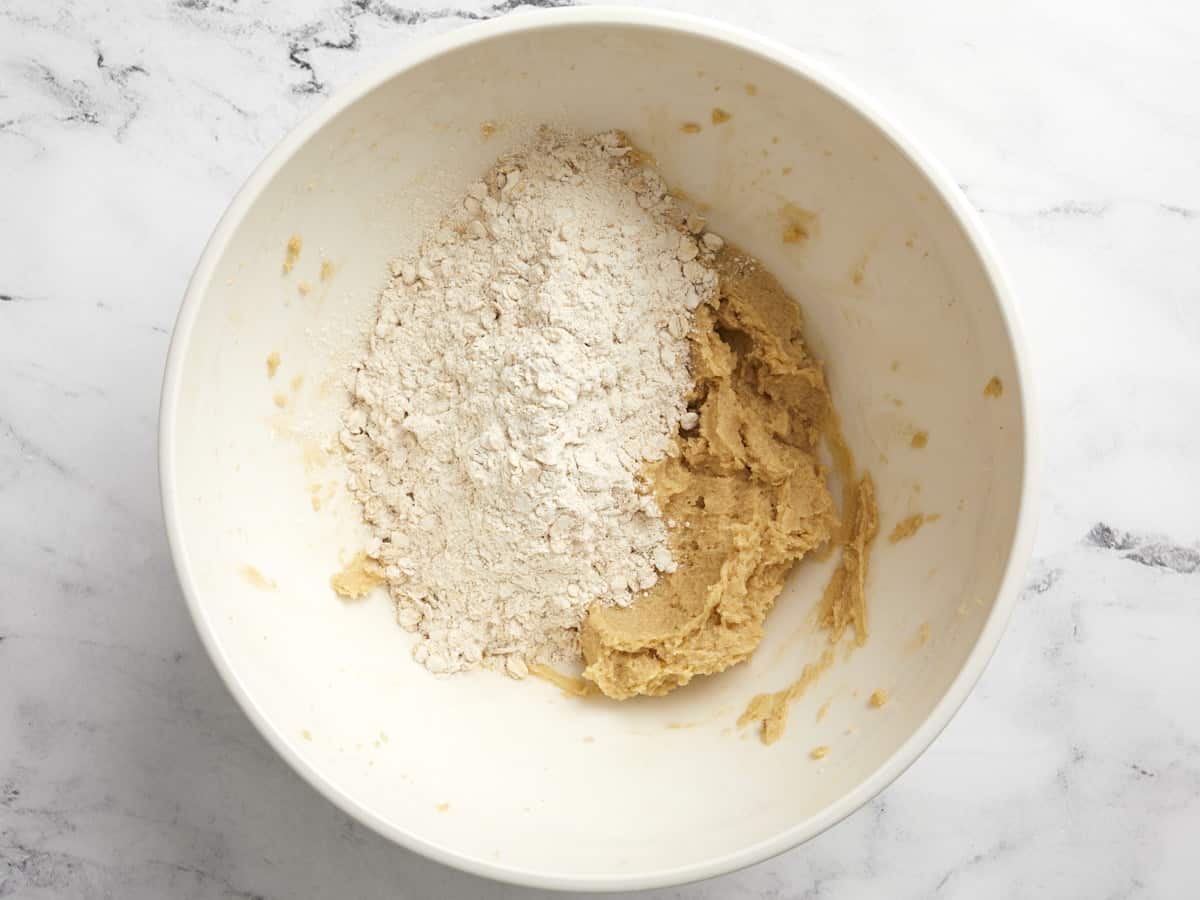 Oat and flour mixture added to butter and sugar mixture in a bowl.