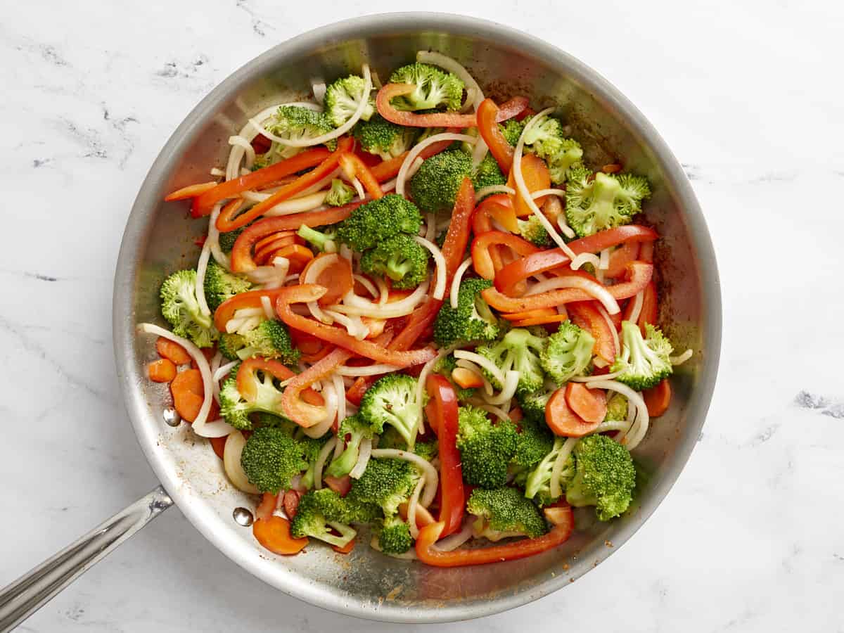 Peppers and onions added to a skillet with broccoli and carrots.