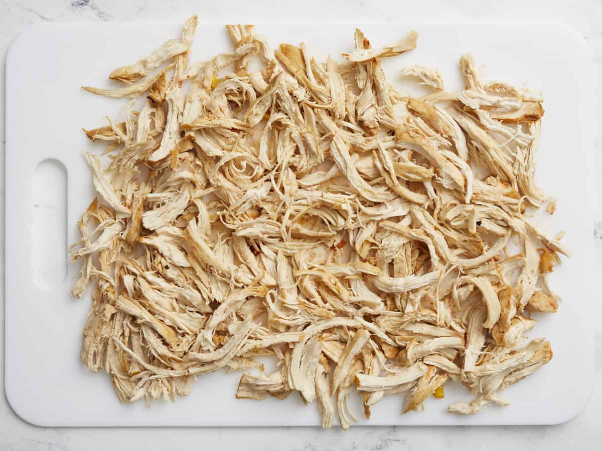 Cooked chicken breasts being shredded on a clean cutting board.