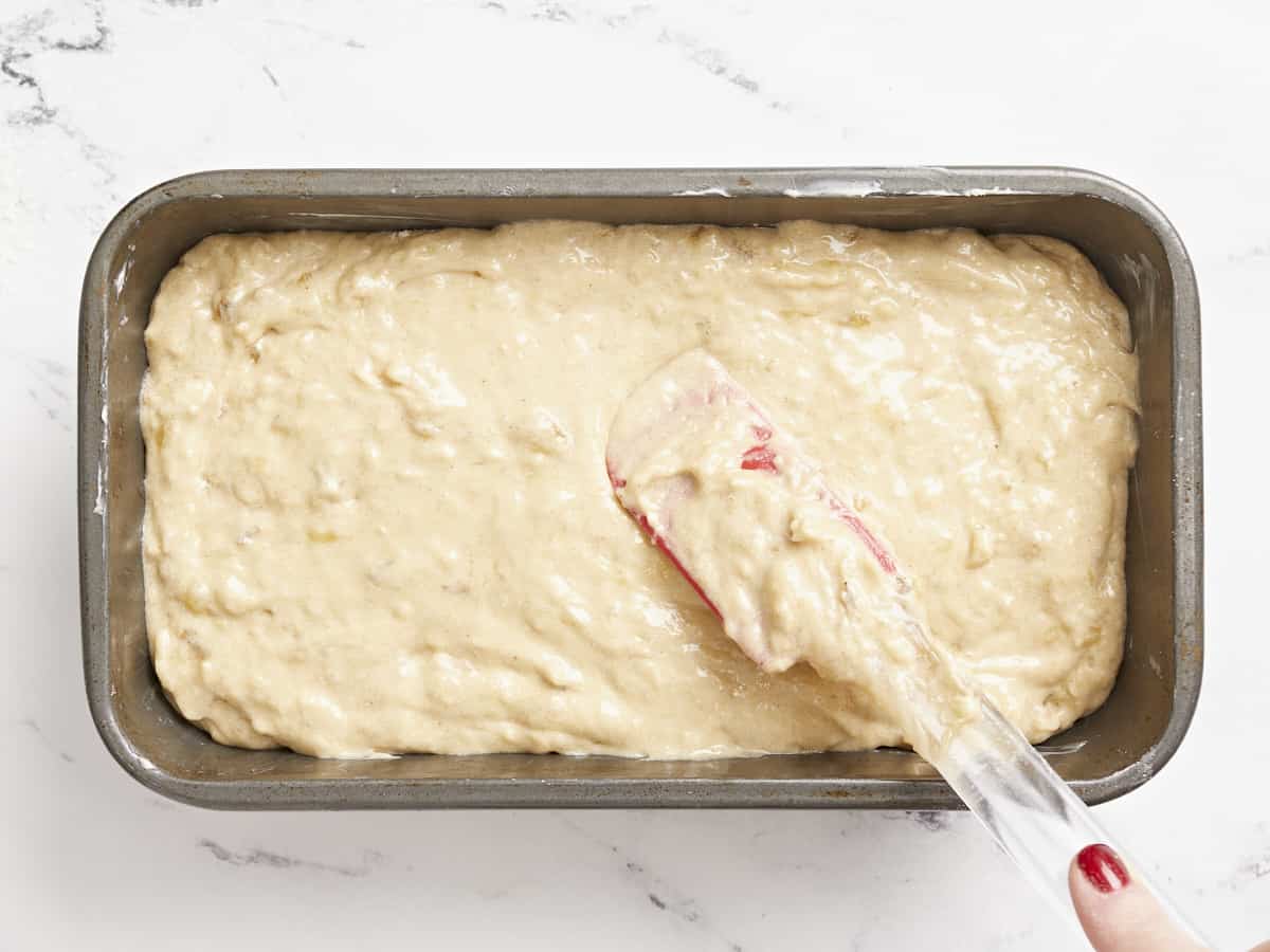 Banana bread batter being smoothed into a bread pan. 