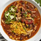 Overhead view of Chicken Enchilada Soup in a white bowl with a black spoon on the side.