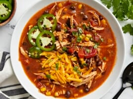 Overhead view of Chicken Enchilada Soup in a white bowl with a black spoon on the side.