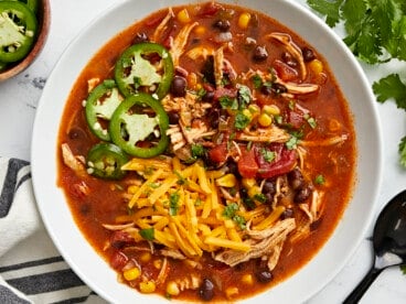 Overhead view of Chicken Enchilada Soup in a white bowl with a black spoon on the side.
