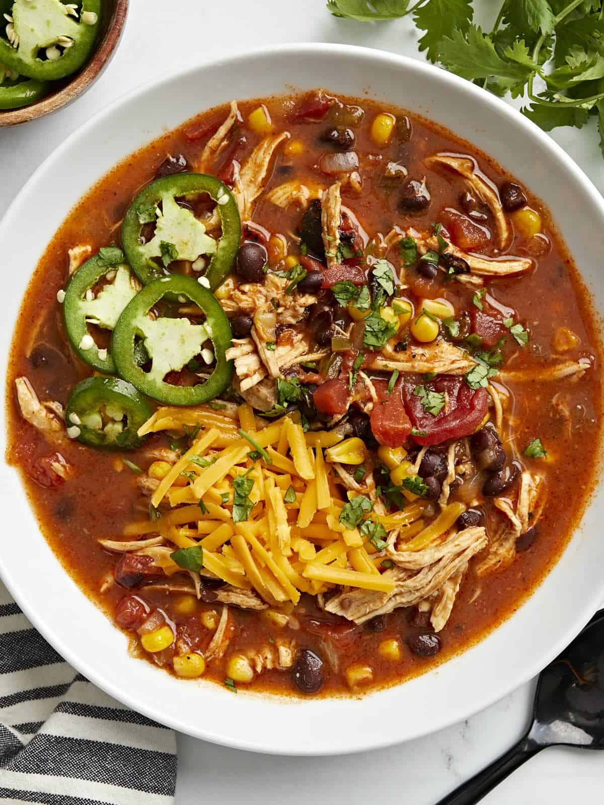 Overhead view of Chicken Enchilada Soup in a white bowl with a black spoon on the side.