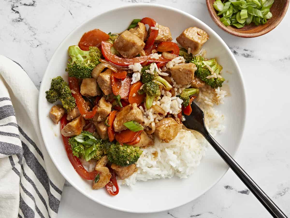 Overhead view of a plate of chicken stir fry with white rice and a fork serving some out.