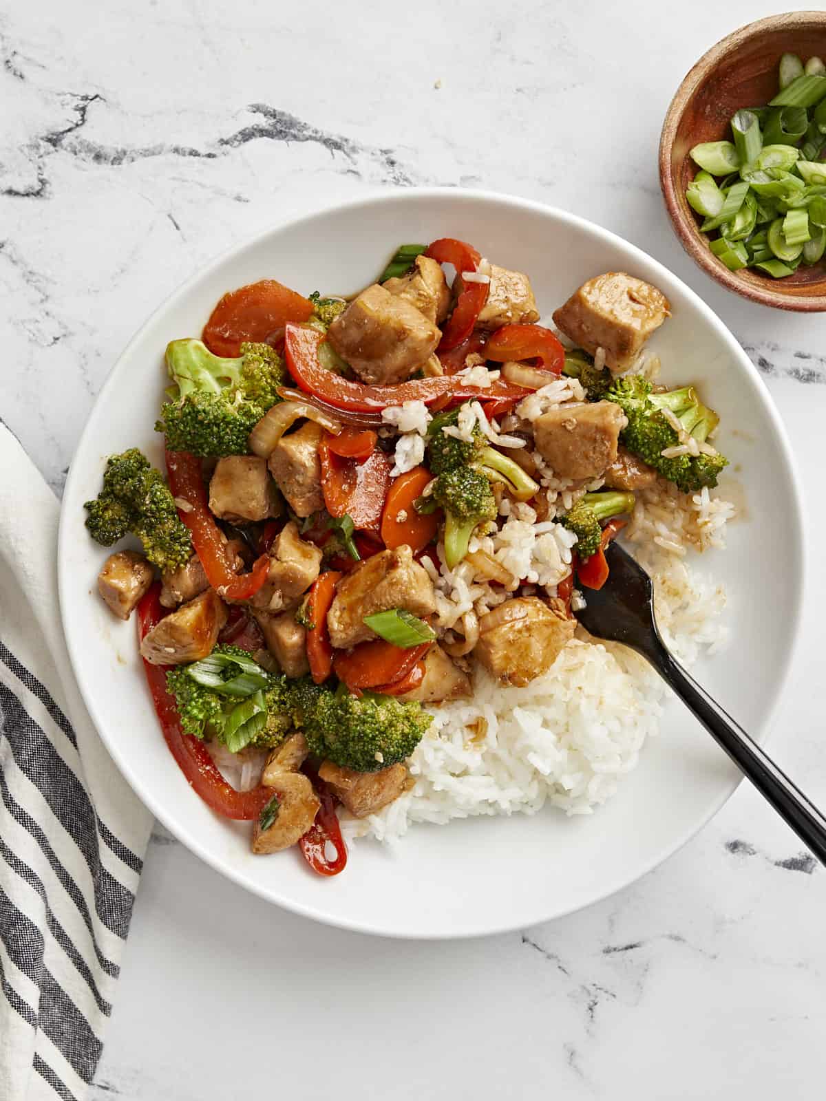Chicken stir fry on a plate with white rice and a fork serving some out.