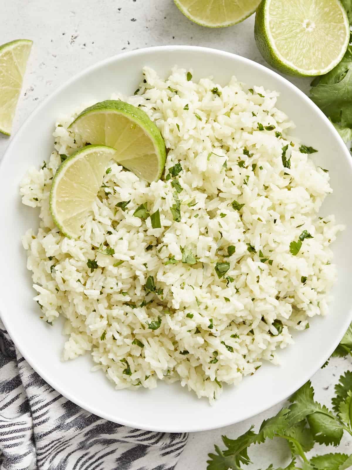 Overhead view of cilantro lime rice in a bowl garnished with lime wedges.