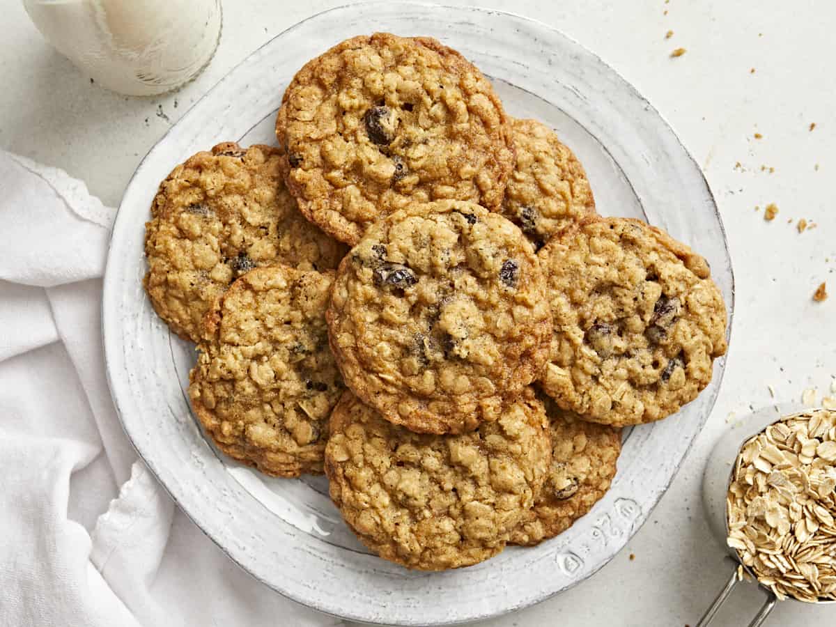 Top view of a stack of oatmeal cookies on a plate with a white napkin and a cup of milk next to it.