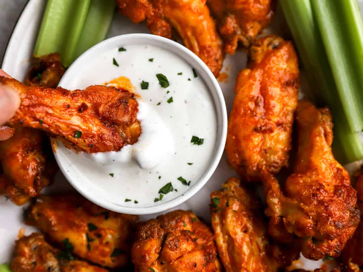 close up view of a buffalo wing dipped in white sauce.