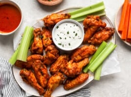 overhead view of buffalo wings on a white platter with celery and white sauce.