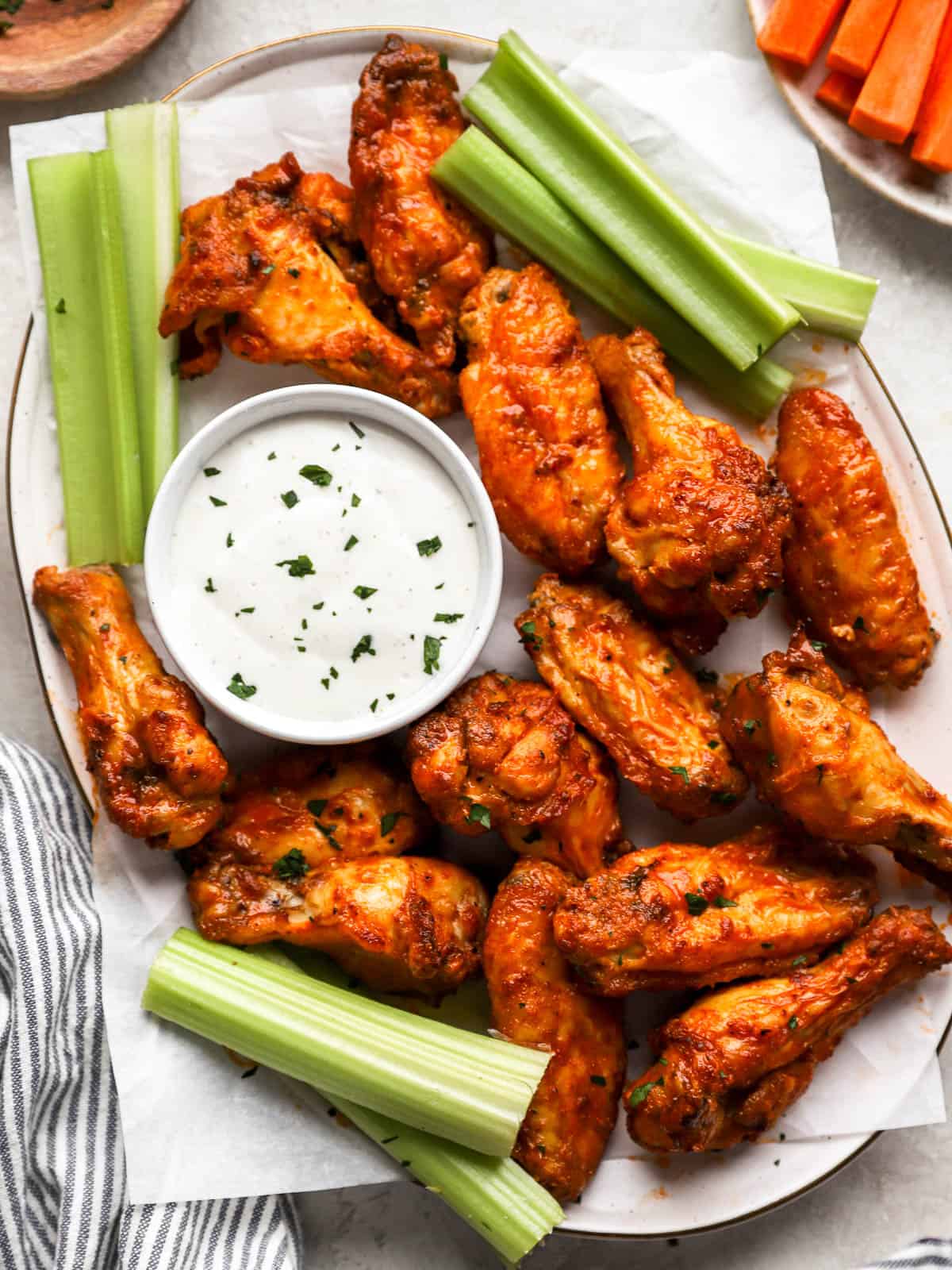 overhead view of buffalo wings on a white platter with celery and white sauce.