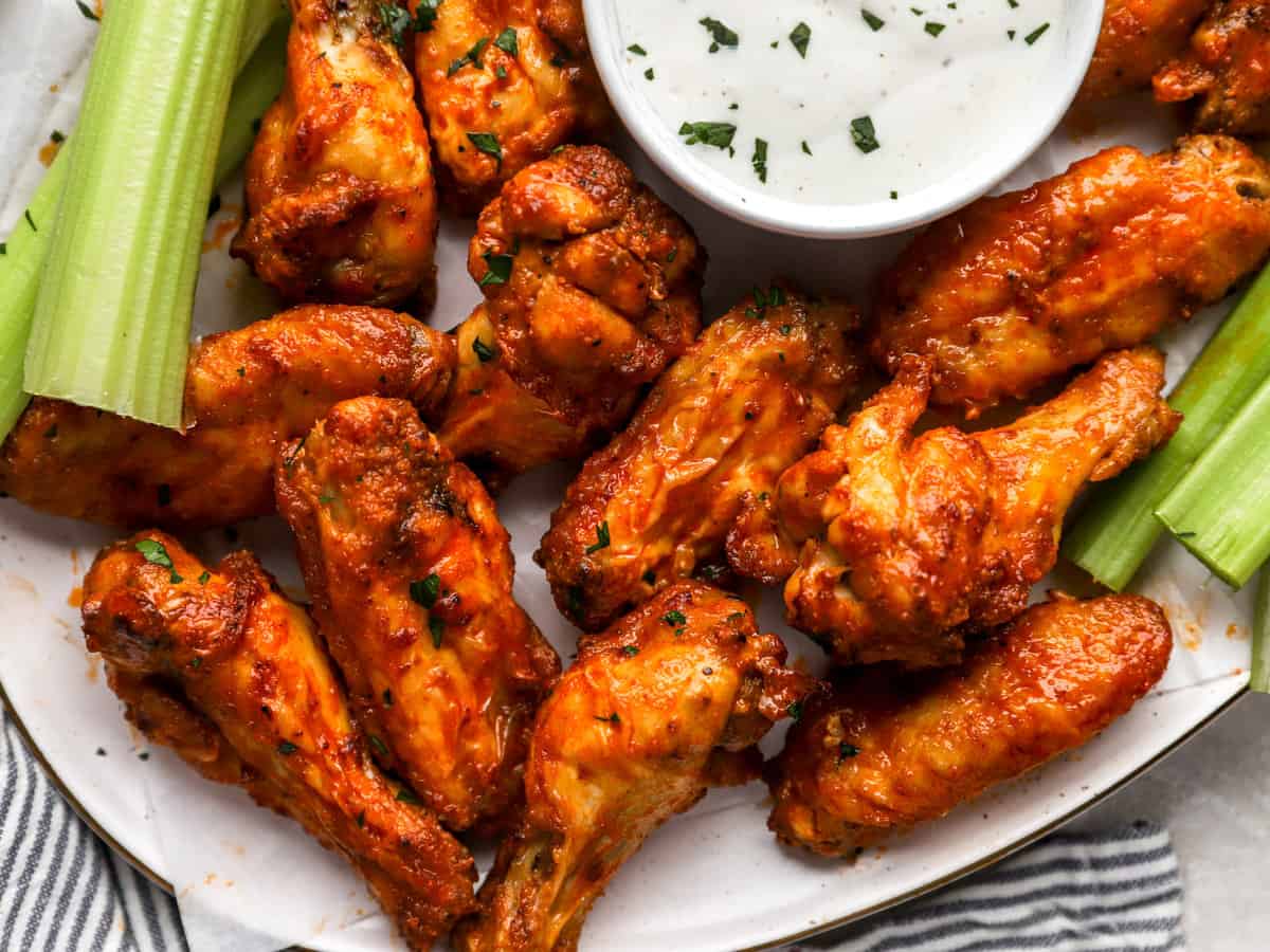 close up view of buffalo wings on a white platter with celery and white sauce.