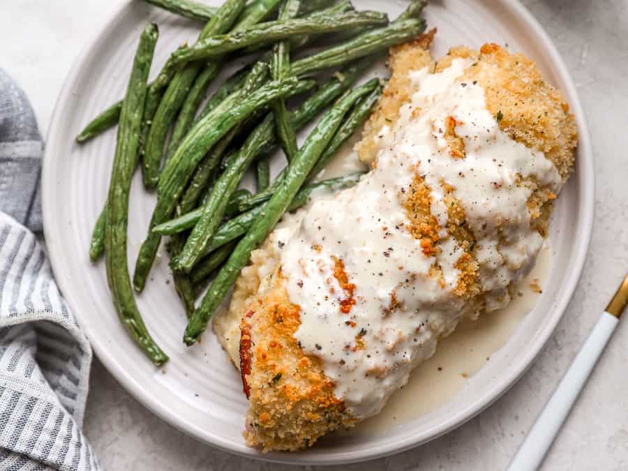 overhead view of chicken cordon bleu covered with sauce on a plate with green beans.