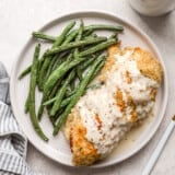 overhead view of chicken cordon bleu covered with sauce on a plate with green beans.