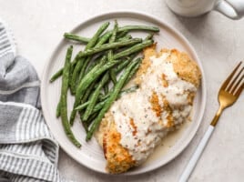 overhead view of chicken cordon bleu covered with sauce on a plate with green beans.