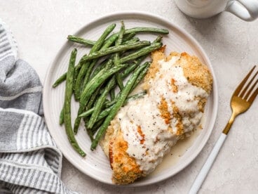 overhead view of chicken cordon bleu covered with sauce on a plate with green beans.