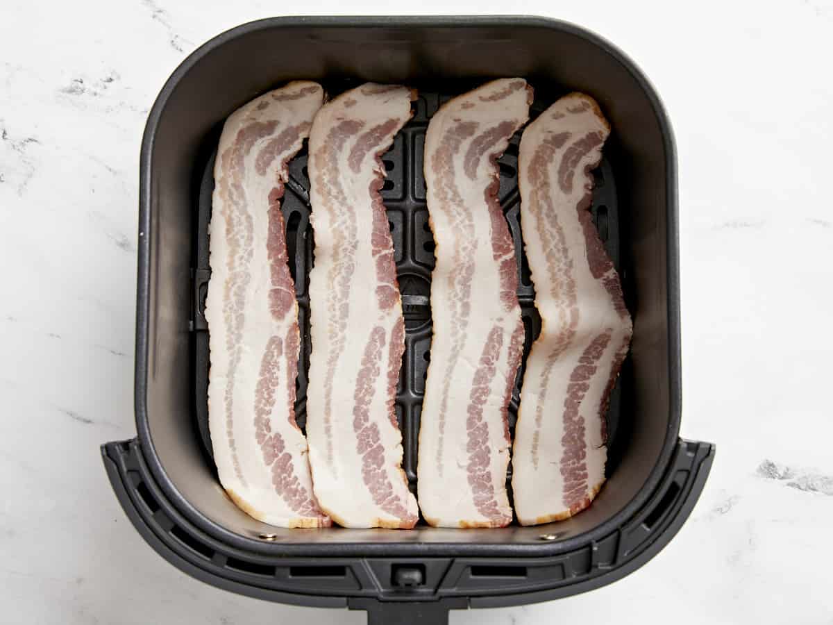 Uncooked bacon in an Air Fryer Basket.