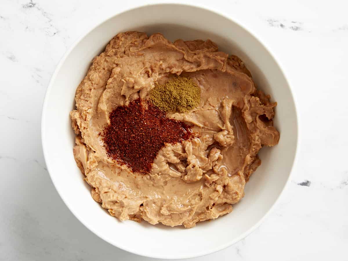 Refried beans in a white mixing bowl with seasoning on top.