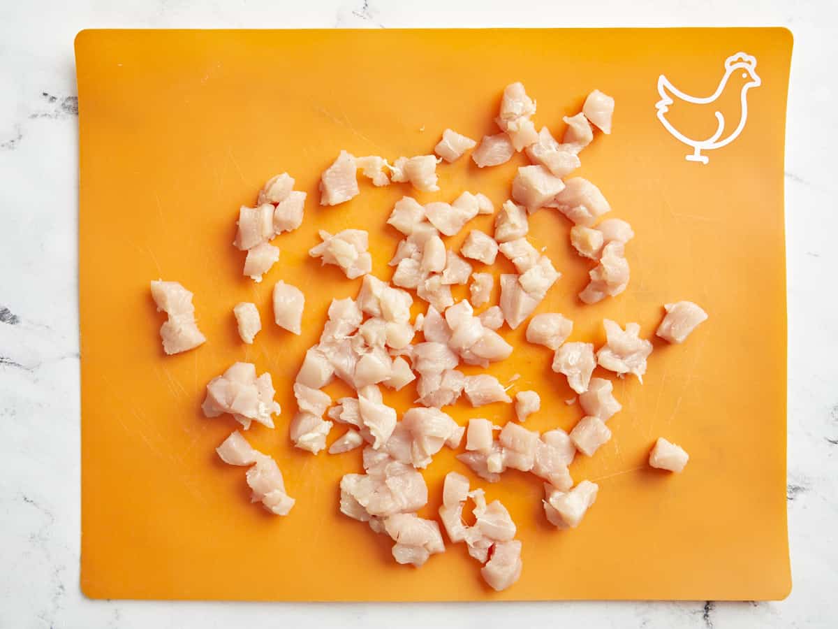 Chicken cubes on an orange cutting board.
