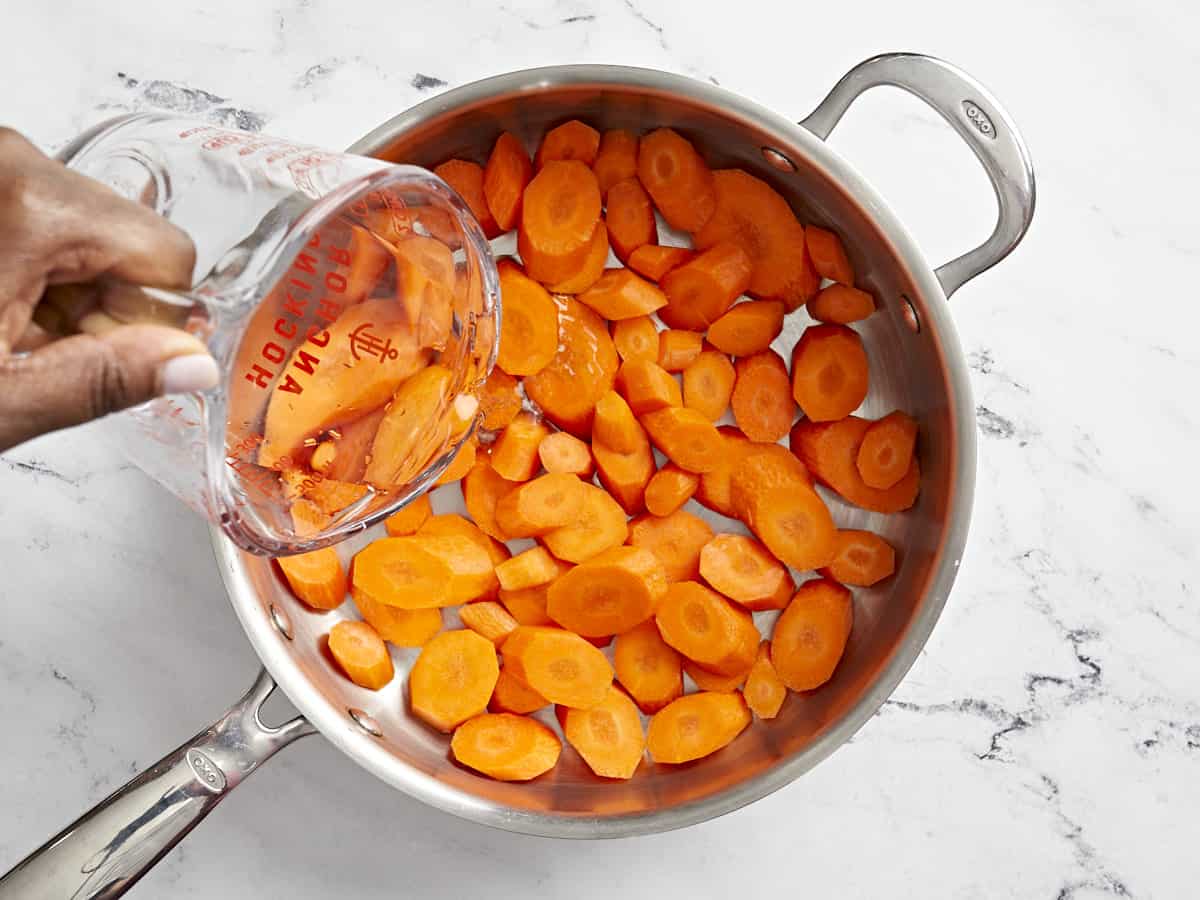 Carrots added to a sauté pan with water.
