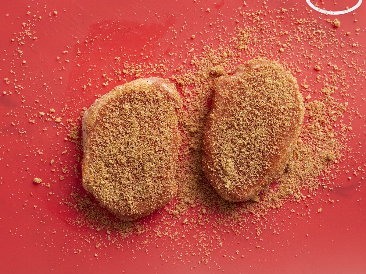 seasoned raw pork chops on a red cutting board.