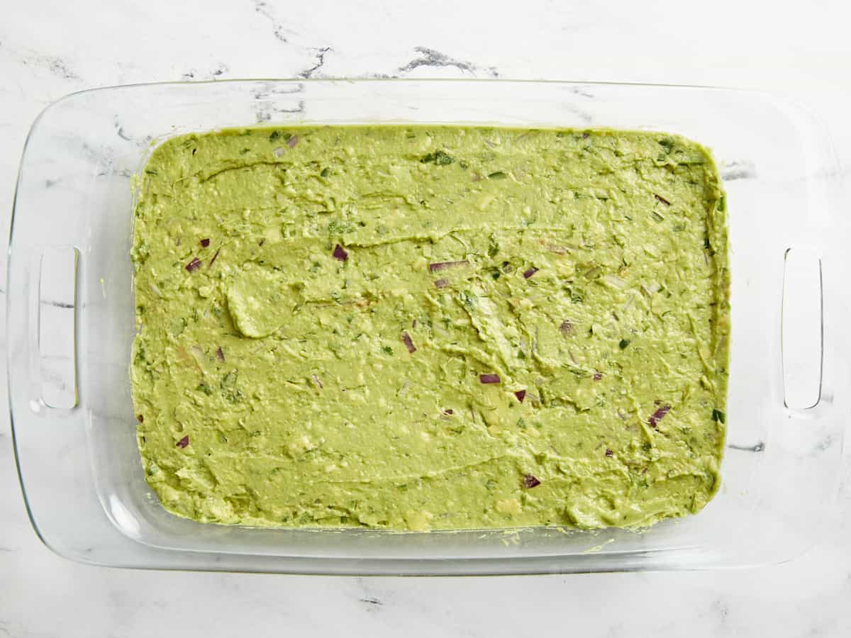 Guacamole spread evenly on top of refried beans in glass casserole dish.