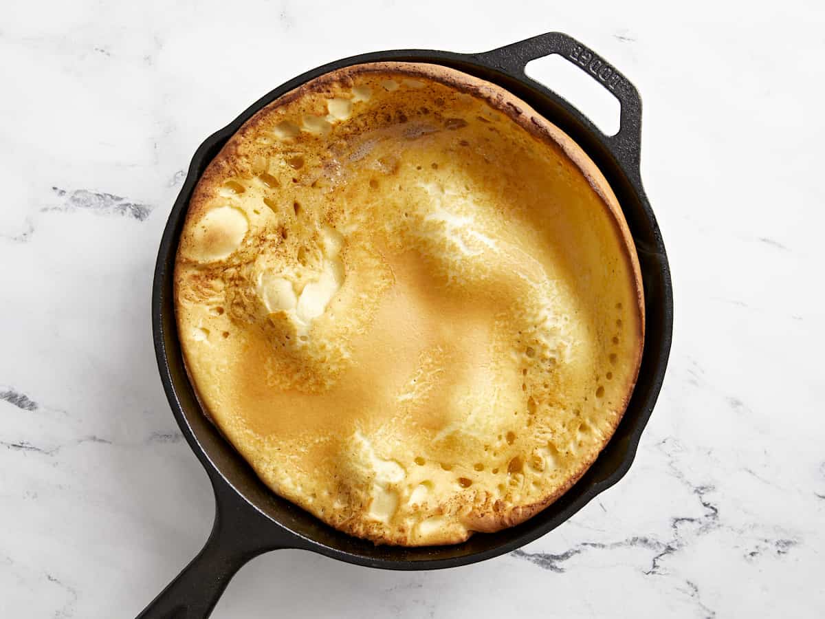 Cooked dutch baby puffed up in a cast iron skillet.