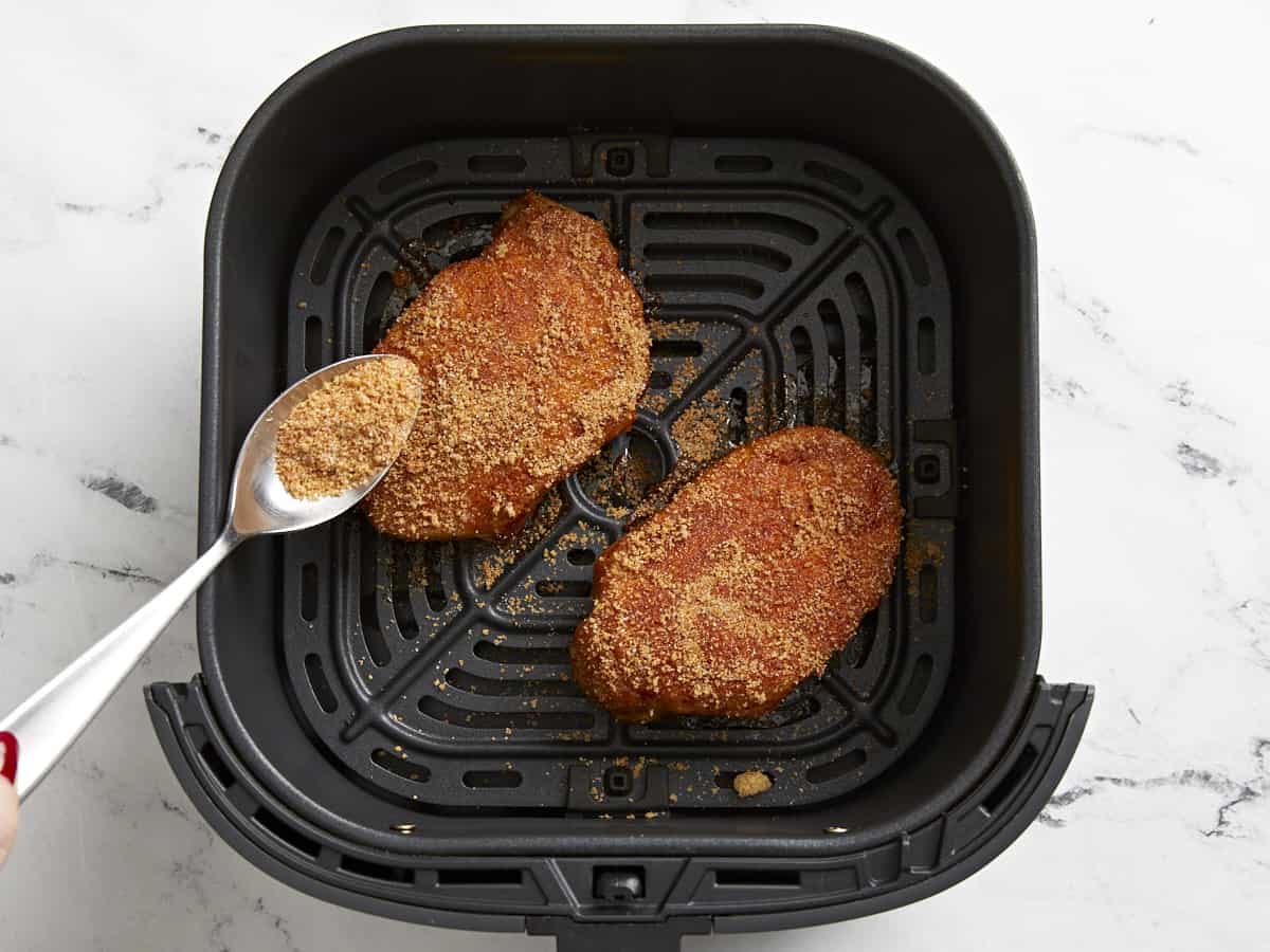 spooning spices over seasoned pork chops in an air fryer basket.