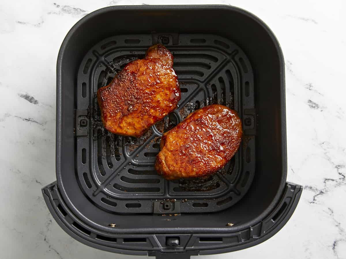 cooked seasoned pork chops in an air fryer basket.