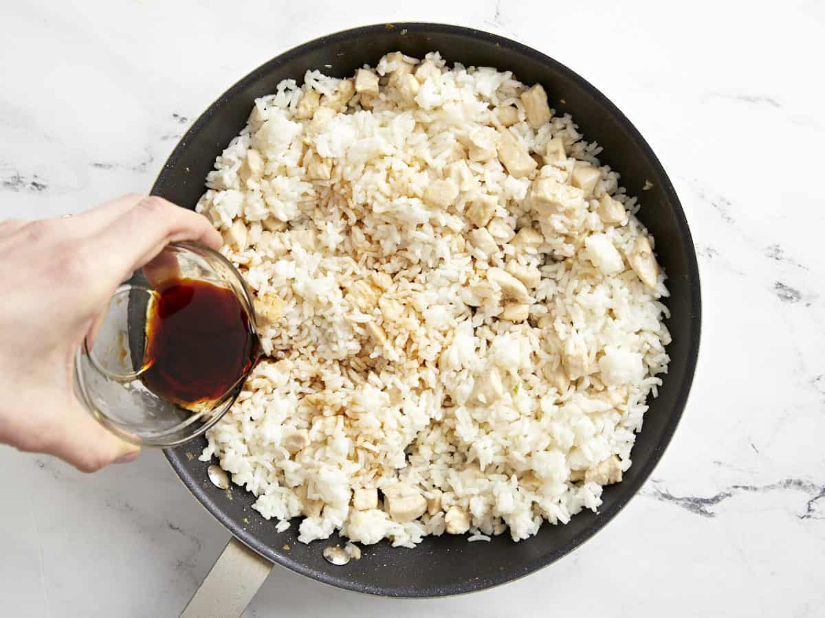 pouring soy sauce over cooked rice in a frying pan.