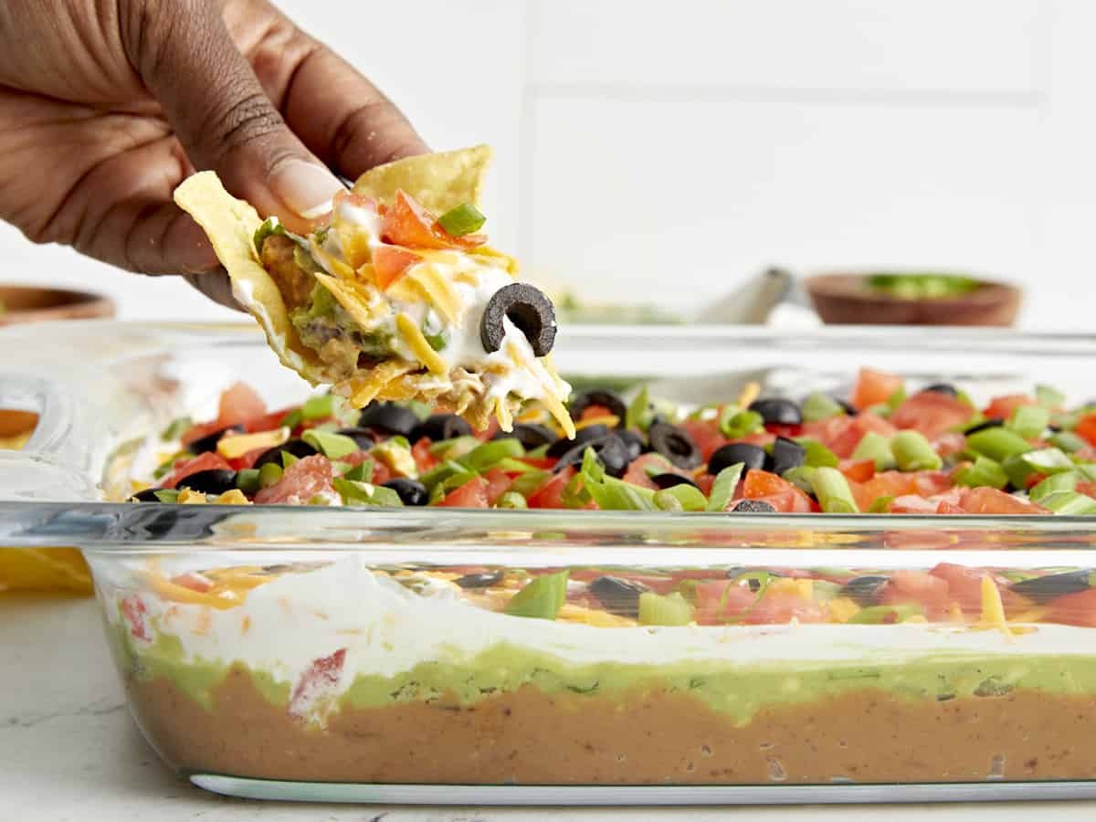 Side view of 7 layer dip with a hand holding a chip and scooping some out.