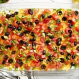 Overhead view of 7 layer dip in a glass casserole dish with a napkin, chips, and lime wedges on the side.