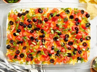 Overhead view of 7 layer dip in a glass casserole dish with a napkin, chips, and lime wedges on the side.