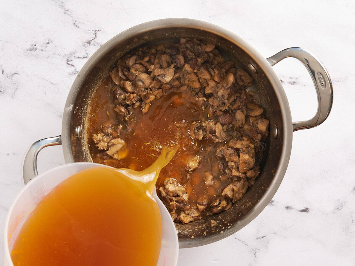 Broth being poured into a pan of sauteed mushrooms.