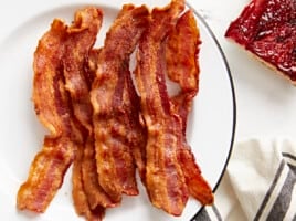 Overhead view of Air Fryer bacon strips on a white serving plate with toast on the side.