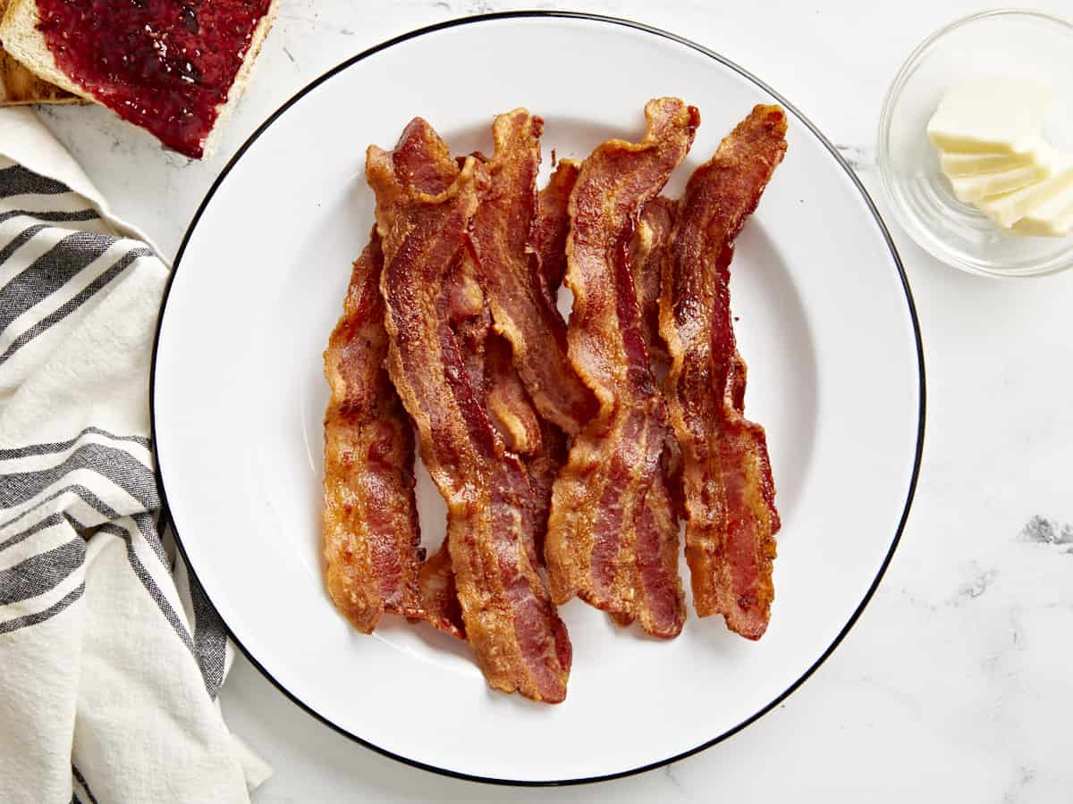 Overhead view of Air Fryer bacon strips on a white serving plate with toast on the side.
