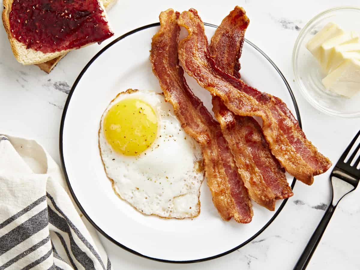 Overhead view of a white plate with Air Fryer Bacon and a fried egg on the plate.