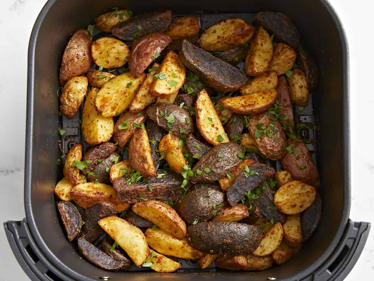 seasoned potatoes in an air fryer basket with herbs.