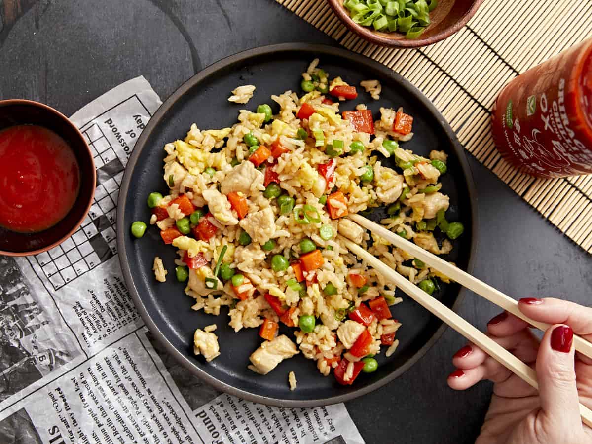 Chopsticks picking up chicken fried rice from a black plate.