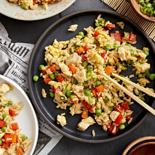 Chopsticks take a bite of chicken fried rice from a black plate.