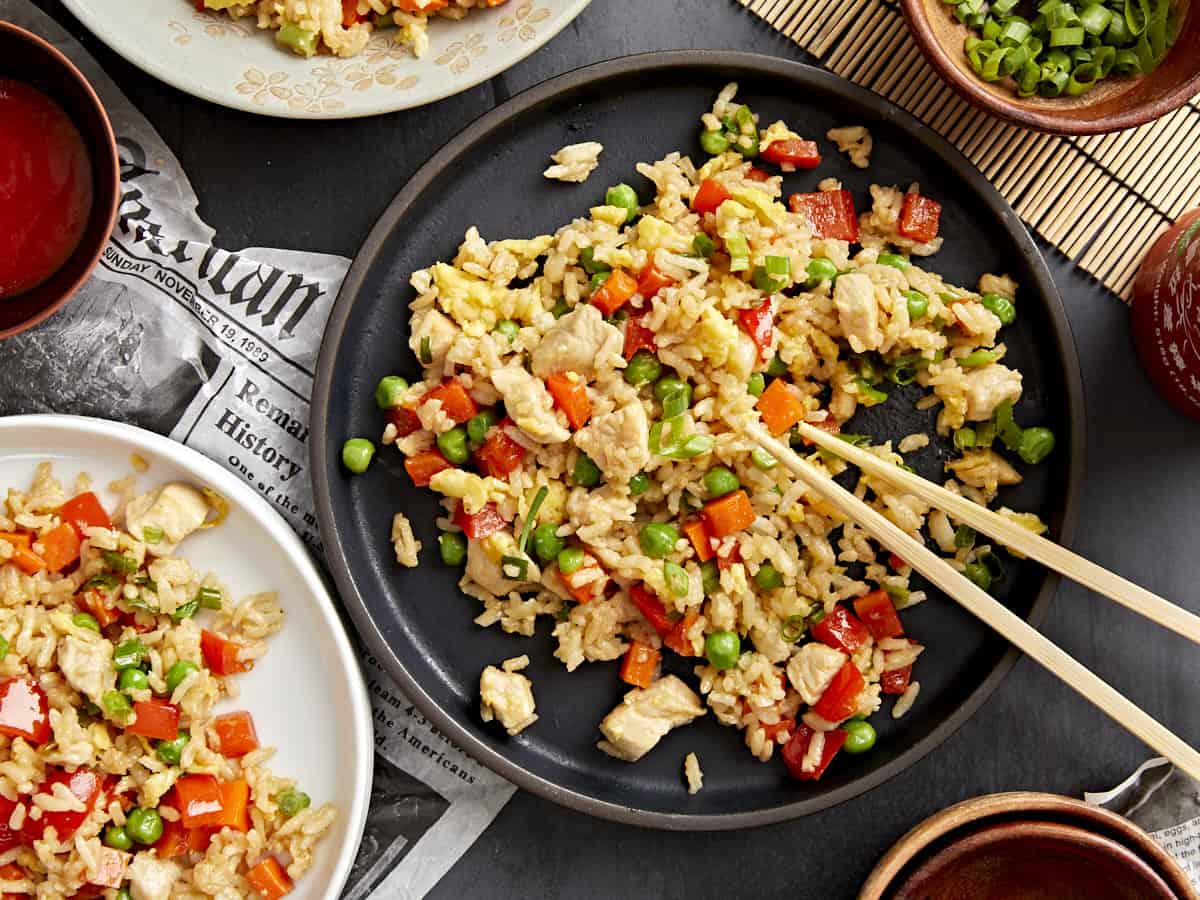 Chopsticks take a bite of chicken fried rice from a black plate.