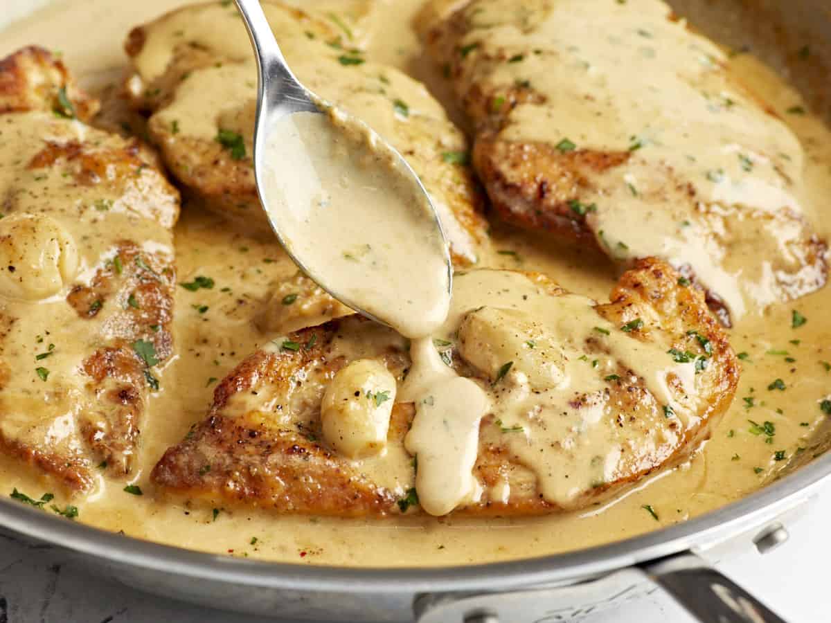 Side close up view of Creamy Garlic Chicken with sauce being spooned over the top of one of the chicken breasts.