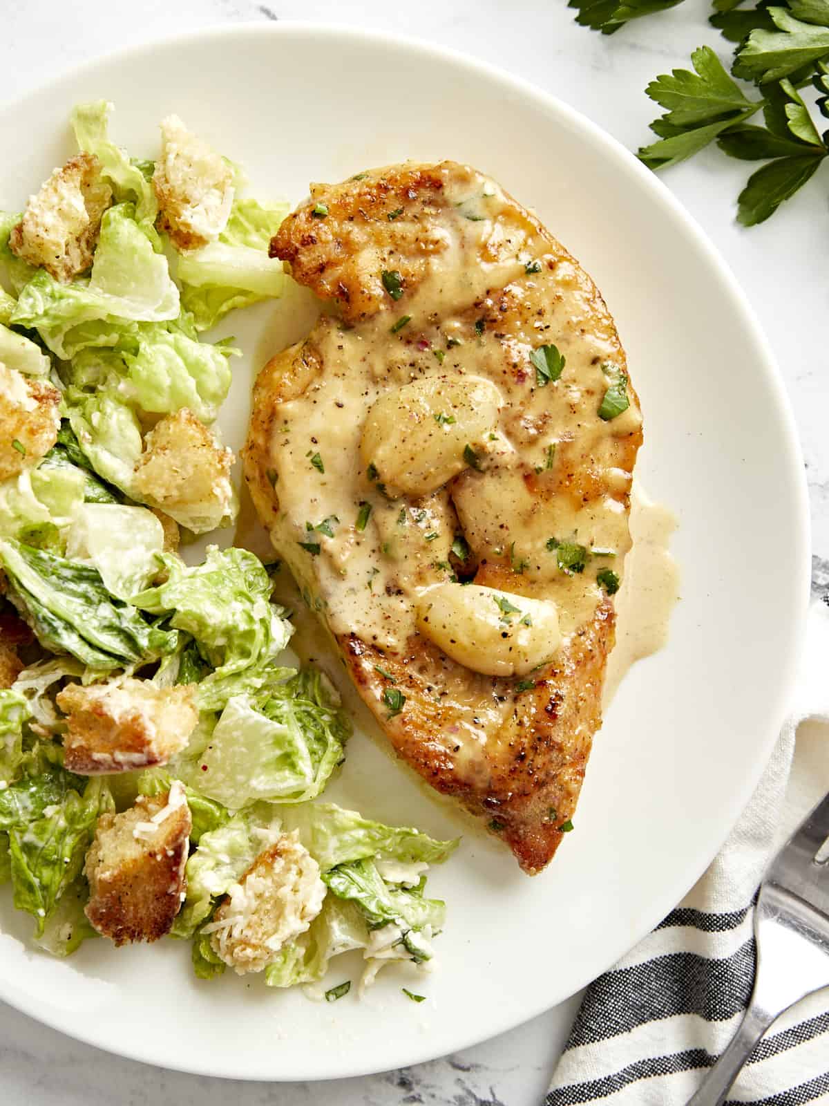 Overhead view of Creamy Garlic Chicken on a white plate served with Caesar Salad.