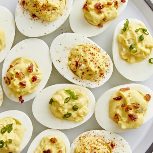 Overhead view of deviled eggs with different toppings on a serving platter.