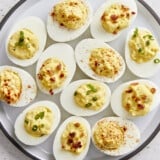 Overhead view of deviled eggs on a platter with different toppings.