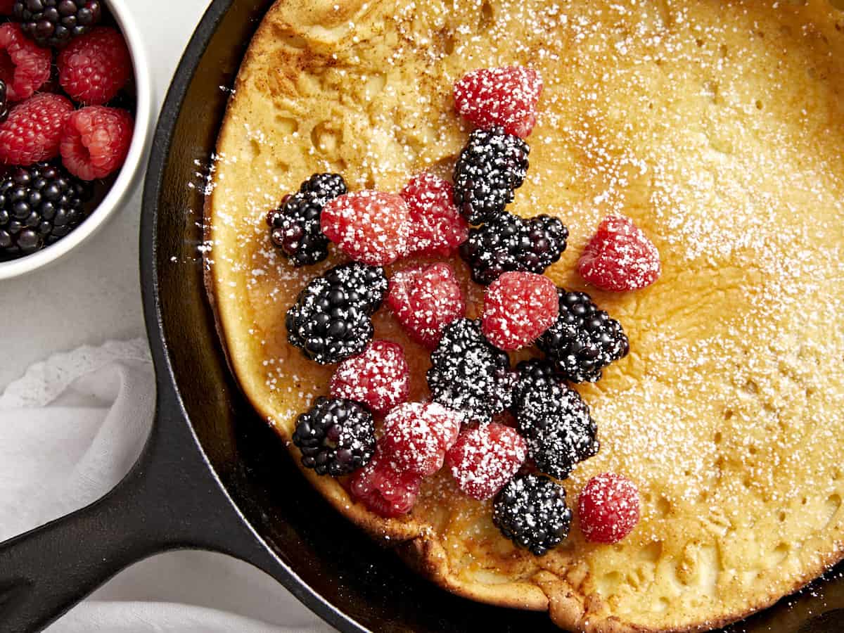 Close up overhead view of a dutch baby in a cast iron skillet with fresh berries on top.