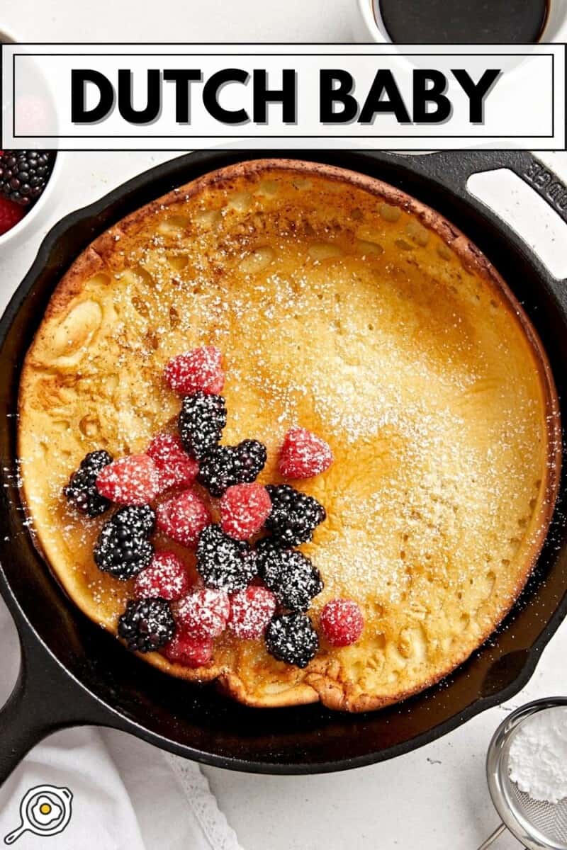 Overhead view of a dutch baby in a cast iron skillet with fresh berries in the center and title text at the top.