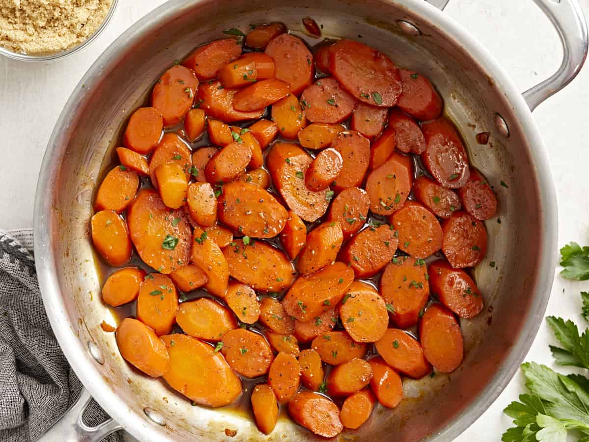 Overhead view of glazed carrots in a sauté pan garnished with chopped parsley.