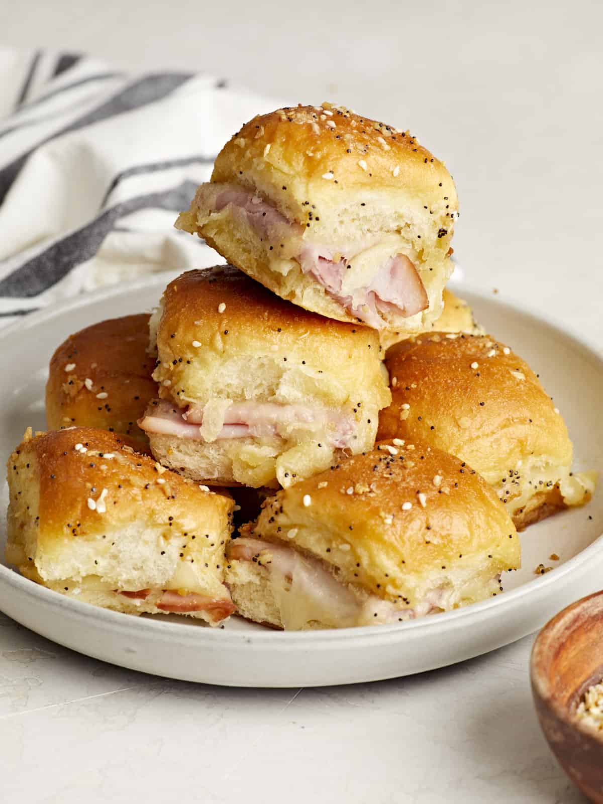 Front side view of a stack of ham and cheese sliders on a plate.